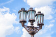 © SergeiPh - Street lamp with three lamps against blue sky.