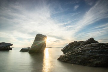 View through rocks on a sandy beach into the sunset. Landscape shot with a view to the horizon over the wide sea on the coast of Ouranoupoli, Thessaloniki, Central Macedonia, Greece