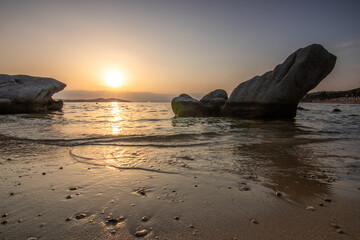 View through rocks on a sandy beach into the sunset. Landscape shot with a view to the horizon over the wide sea on the coast of Ouranoupoli, Thessaloniki, Central Macedonia, Greece