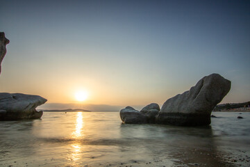 View through rocks on a sandy beach into the sunset. Landscape shot with a view to the horizon over the wide sea on the coast of Ouranoupoli, Thessaloniki, Central Macedonia, Greece