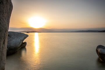 View through rocks on a sandy beach into the sunset. Landscape shot with a view to the horizon over the wide sea on the coast of Ouranoupoli, Thessaloniki, Central Macedonia, Greece