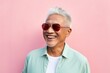 © Markus Schröder - Portrait of a grinning asian man in his 70s wearing a trendy sunglasses over solid pastel color wall