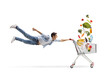 © Ljupco Smokovski - Full length shot of a casual guy man flying and holding a shopping cart with products falling