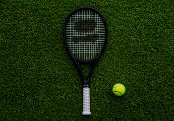 Black tennis racket with a white handle and a tennis ball on a green grass background.