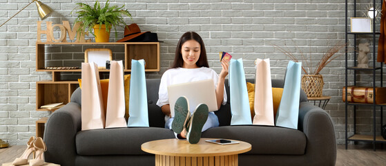 Poster - Young Asian woman with credit cards and laptop shopping online at home