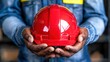 © weerasak - Red hard hat held by a worker, symbolizing safety in construction and industrial work.