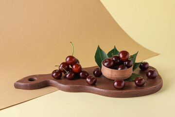 Wooden board and bowl with sweet cherries on colorful background