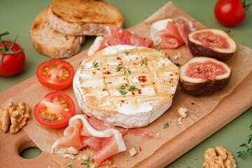 Wooden board with tasty baked Camembert cheese on green background