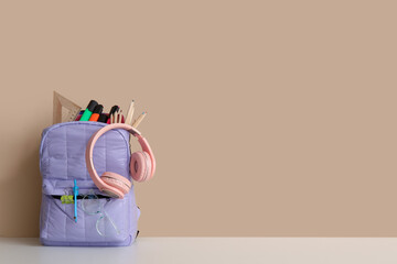 Wall Mural - Lilac school backpack with different stationery and headphones on white table near orange wall