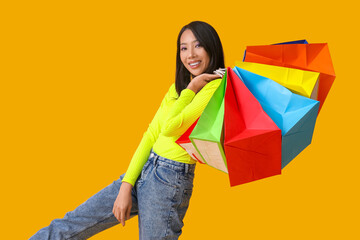 Sticker - Young Asian woman with shopping bags on yellow background