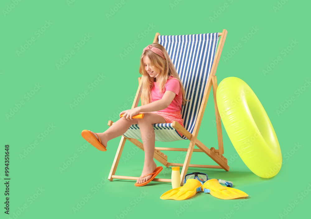 Beautiful girl spraying her lags while sitting on deck chair on green background