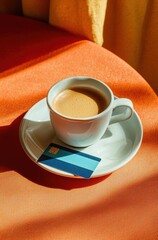 minimalist orange table setting featuring a blue card and a coffee cup with latte art in bright sunl