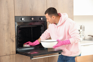 Poster - Young man with sponge and bowl cleaning oven in kitchen