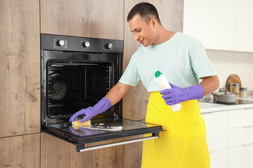 Poster - Young man with sponge and detergent cleaning oven in kitchen