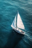 Aerial view of a sailboat gliding across calm blue waters on a sunny day