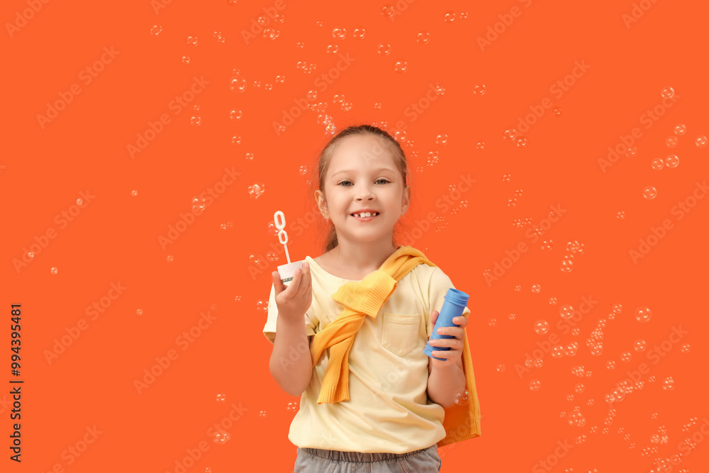Cute little girl with soap bubbles wand on orange background