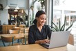 © Athena  - Smiling Woman Working on Laptop in Cafe