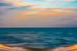 © Hanna Tor - Blurred view of the ocean at sunset with soft waves and colorful sky.