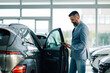 © Zamrznuti tonovi - Businessman in suit examining car in dealership with digital device.