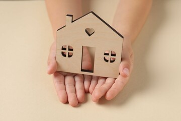 Wall Mural - Adoption concept. Kid with cutout of house at beige table, closeup