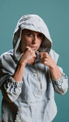 Wall Mural - Vertical video Strong bold woman flexing muscles and throwing punches in studio, street fight boxing concept against blue background. Violent confident person prepared to start fighting. Camera A.