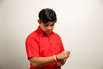 Asian man is tying red and white ribbon to celebrate Indonesia's independence day on August 17 wearing red top and flag headband isolated on white background