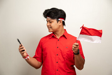 Excited young Asian men celebrate Indonesian independence day on 17 August by holding the Indonesian flag isolated over white background