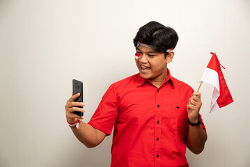 Excited young Asian men celebrate Indonesian independence day on 17 August while holding the Indonesian flag and mobile phone isolated over white background