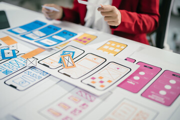 Web designer is reviewing mobile application wireframes at their desk, deciding which design elements will offer the best user experience