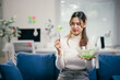© Parichat - Young businesswoman looks disgusted while eating salad in her home office, showing her commitment to a healthy diet