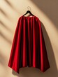 © Sanwa - A red cape hangs gracefully on a black hanger, its rich color contrasting beautifully with the beige background, symbolizing power, passion, royalty, and elegance.