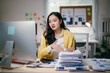 © Parichat - Focused businesswoman in yellow suit jacket manages paperwork at desk, working diligently on computer in office. Shows resilience and determination in corporate world