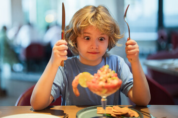 Wall Mural - Funny surprised Little boy eating seafood in cafe. Kid eat Food fish gourmet seafood shrimp in restaurant. Adorable little boy at restaurant having breakfast.