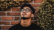© avaye - Portrait of a young man with glasses looking upwards, standing against a brick wall, conveying a thoughtful or contemplative mood