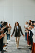 © Jacob Lund - Successful female leader walking between supportive colleagues clapping in appreciation at a business meeting in a modern office setting.