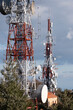 © yaqui_villegas - Two tall transmission towers with multiple antennas and satellite dishes stand amidst a natural environment, under a partly cloudy sky.
