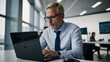 © Tengkwa - Focused Businessman:  A serious, mature businessman concentrates intently on his laptop in a modern, bright office setting.  The image conveys professionalism, dedication, and strategic thinking.