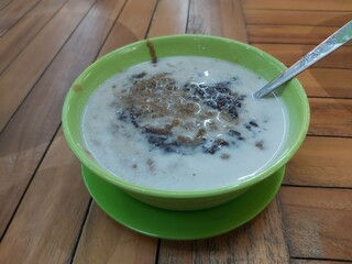 A traditional Indonesian dessert made by green bean porridge and black sticky rice with coconut milk topping in a green bowl