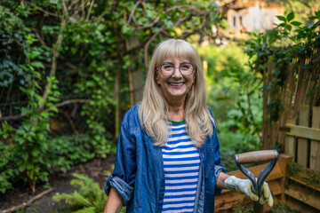 Senior woman standing with a pitchfork in front of the compost heap in the garden