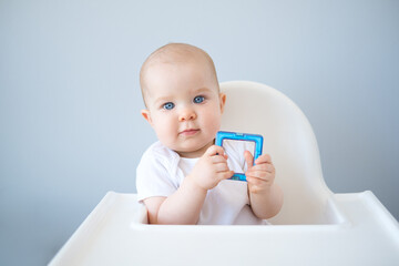 portreit of baby with blue eyes sitting in baby chair playing with toy