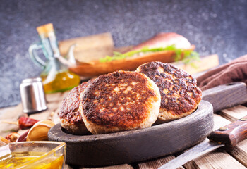 Cooked fried fish cutlets in a plate, on a light wooden table.