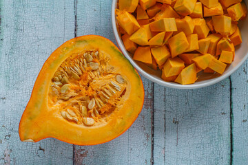 half hokkaido pumpkin with diced pieces in bowl on rustic wood
