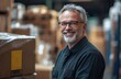 © Rufino - A man with glasses is smiling in front of a stack of boxes