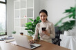 © itchaznong - Young Professional Woman Working Remotely from Home Office Using Laptop and Smartphone