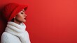 ©  Shomixer - A person wearing a knitted red hat and white scarf, standing against a vibrant red background, evoking a cozy and festive winter scene.