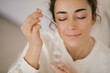 © polinaloves - Young woman 30 years old applying face oil on her skin.