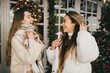 © polinaloves - Two women friends walking on festive decorated city street, having fun together.