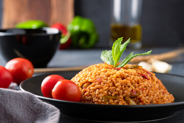 Turkish traditional food tomato bulgur pilaf on black stone table