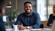 © sungedi - A smiling African American man sitting at a table in an office, looking at the camera