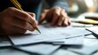 © AucArtStudio - Person writing notes on paper with a yellow pencil in a workspace setting.